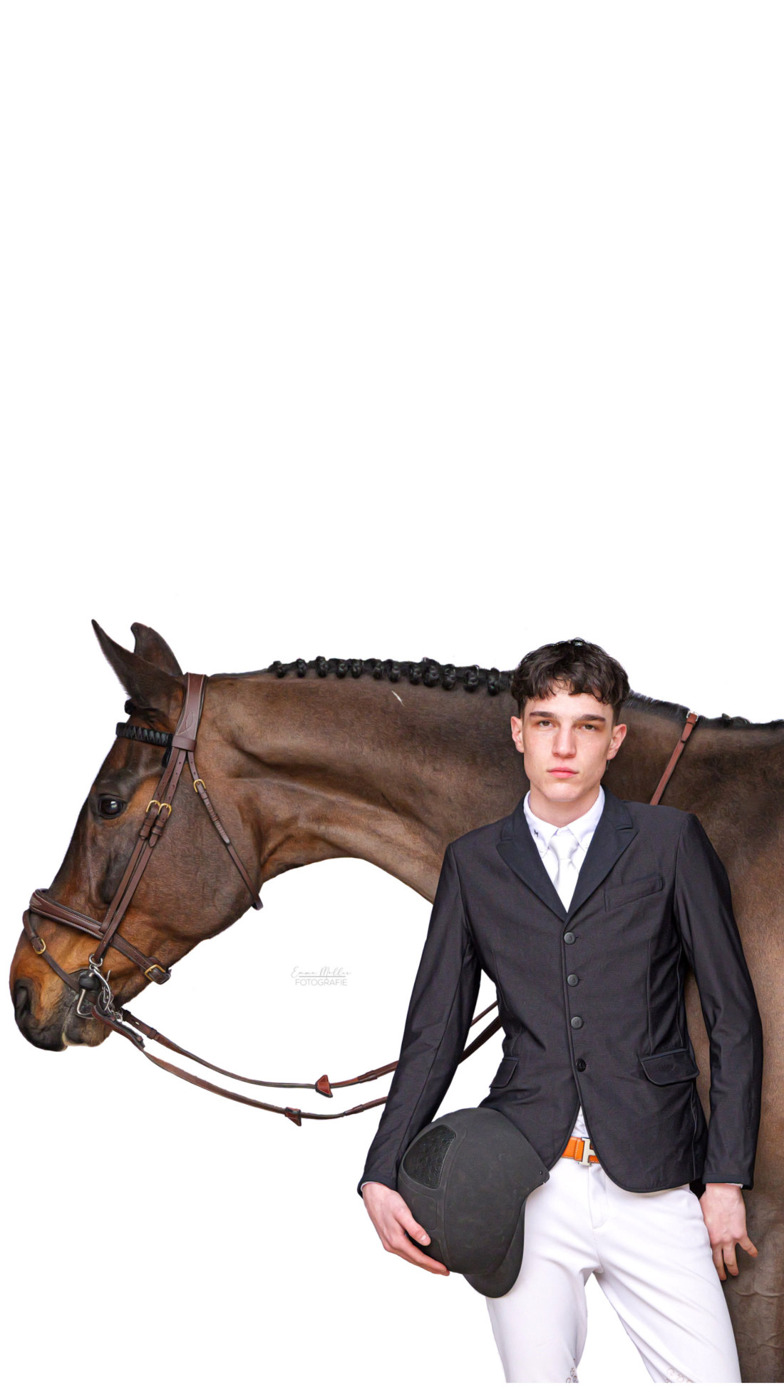 Young rider in a dark show jacket and white breeches holding a helmet in front of a bay horse